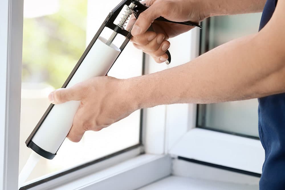 Hands applying sealant around a window frame