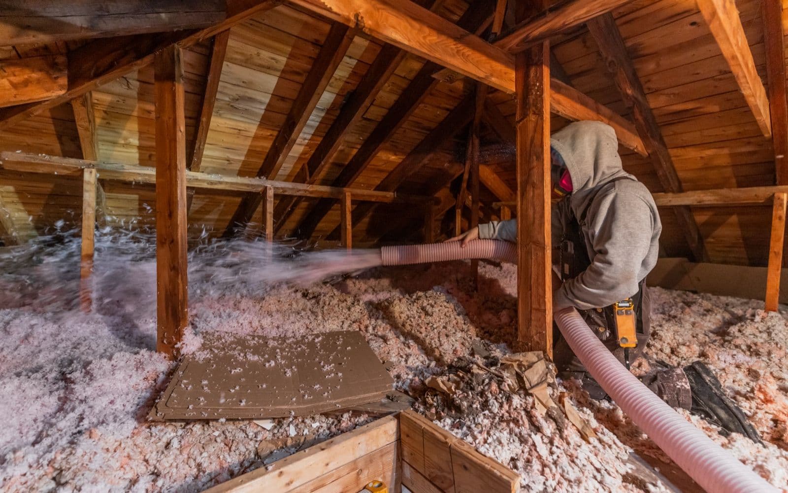 Technician blowing insulation into an attic, under the roof framing